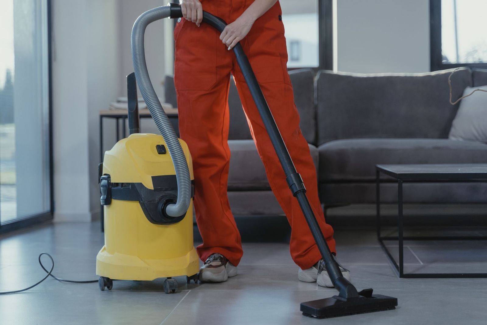 Reinigungskraft in roter Arbeitskleidung reinigt einen Teppich im Wohnzimmer